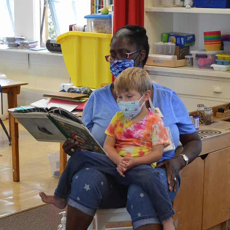 Image of a JCC Berkeley Preschool teacher reading a book to a preschool student. Click on the image to view the JCC Preschool program page.